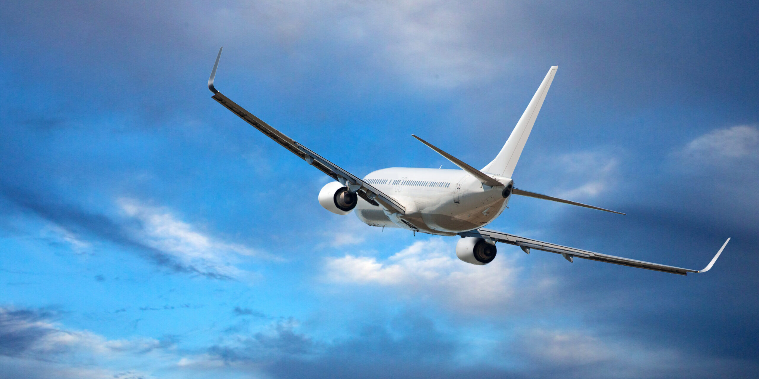 White passenger wide-body plane. Aircraft is flying in blue cloudy sky